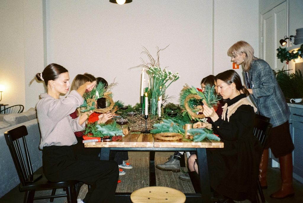 Women crafting Christmas wreaths at a indoor holiday workshop.