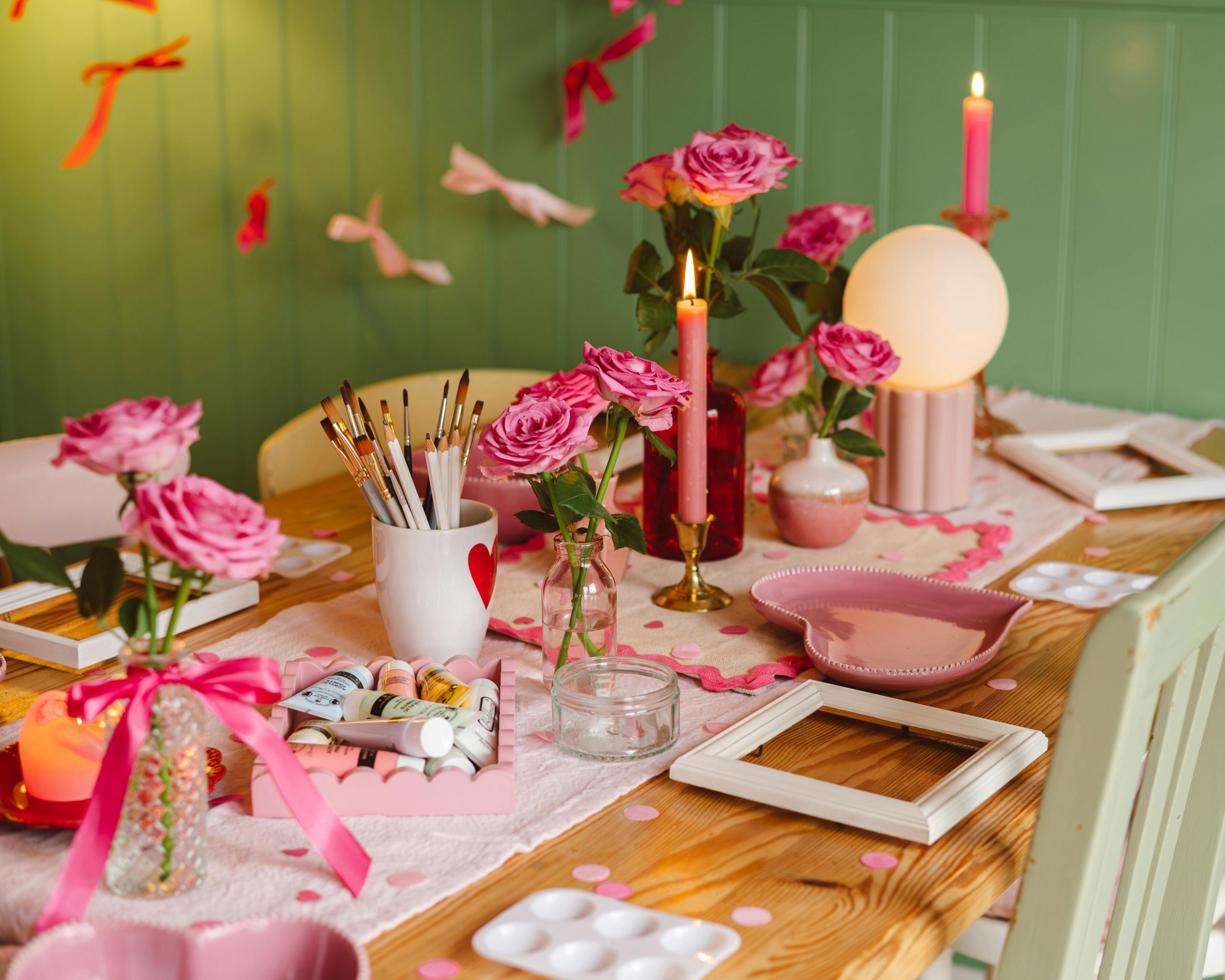 A beautifully decorated table for a craft night with pink roses, candles, and art supplies.